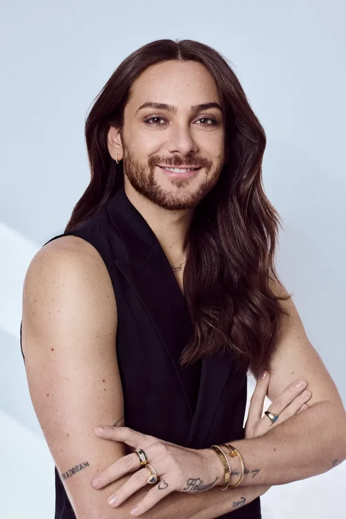 Mann mit langen Haaren und Bart lächelt.