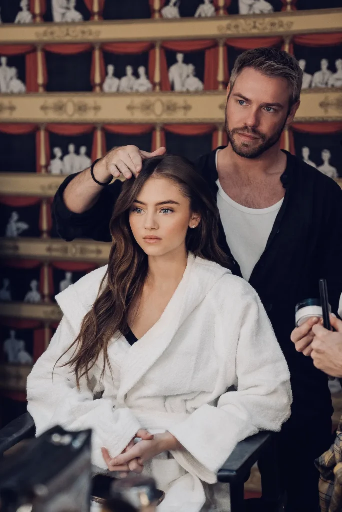 Friseur richtet Haar einer jungen Frau im Bademantel.