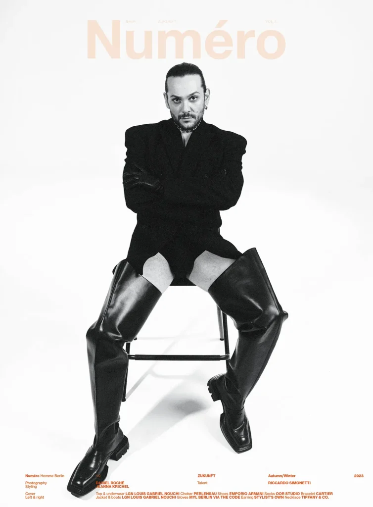 Mann in schwarzem Outfit und Stiefeln sitzt auf Stuhl.