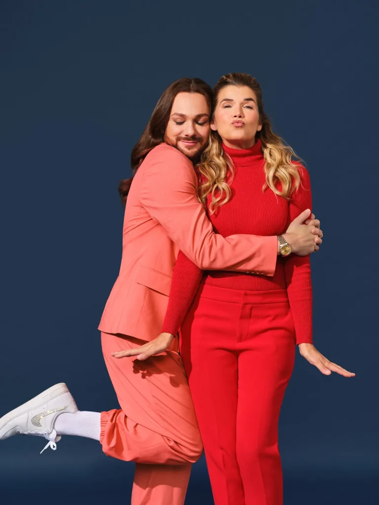 Zwei Personen in roten und korallfarbenen Anzügen umarmen sich.